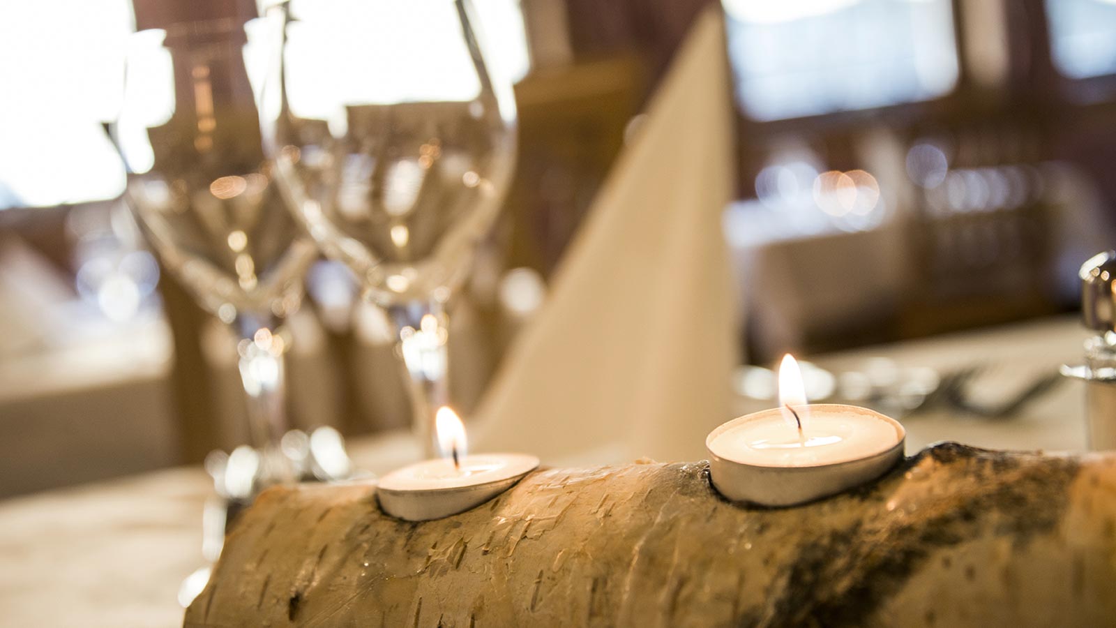 Decorazione da tavola fatta in legno con candele accese e calici di vetro sullo sfondo