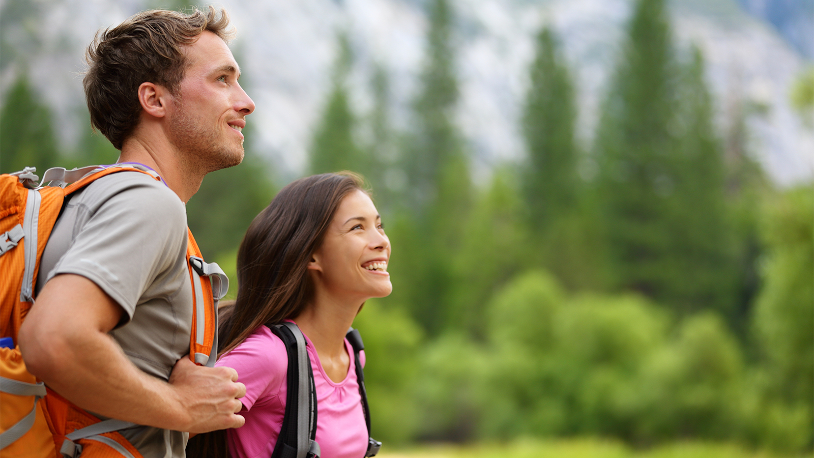 Couple - active hikers hiking enjoying view looking at mountain forest landscape in Yosemite National Park, California, USA. Happy multiracial outdoors couple, young Asian woman and Caucasian man.