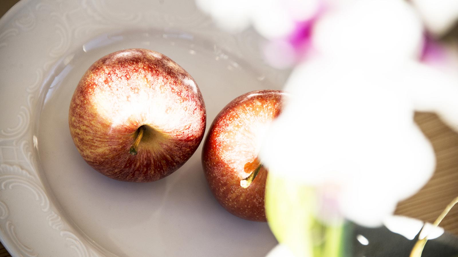 Dish with two red apples illuminated by daylight