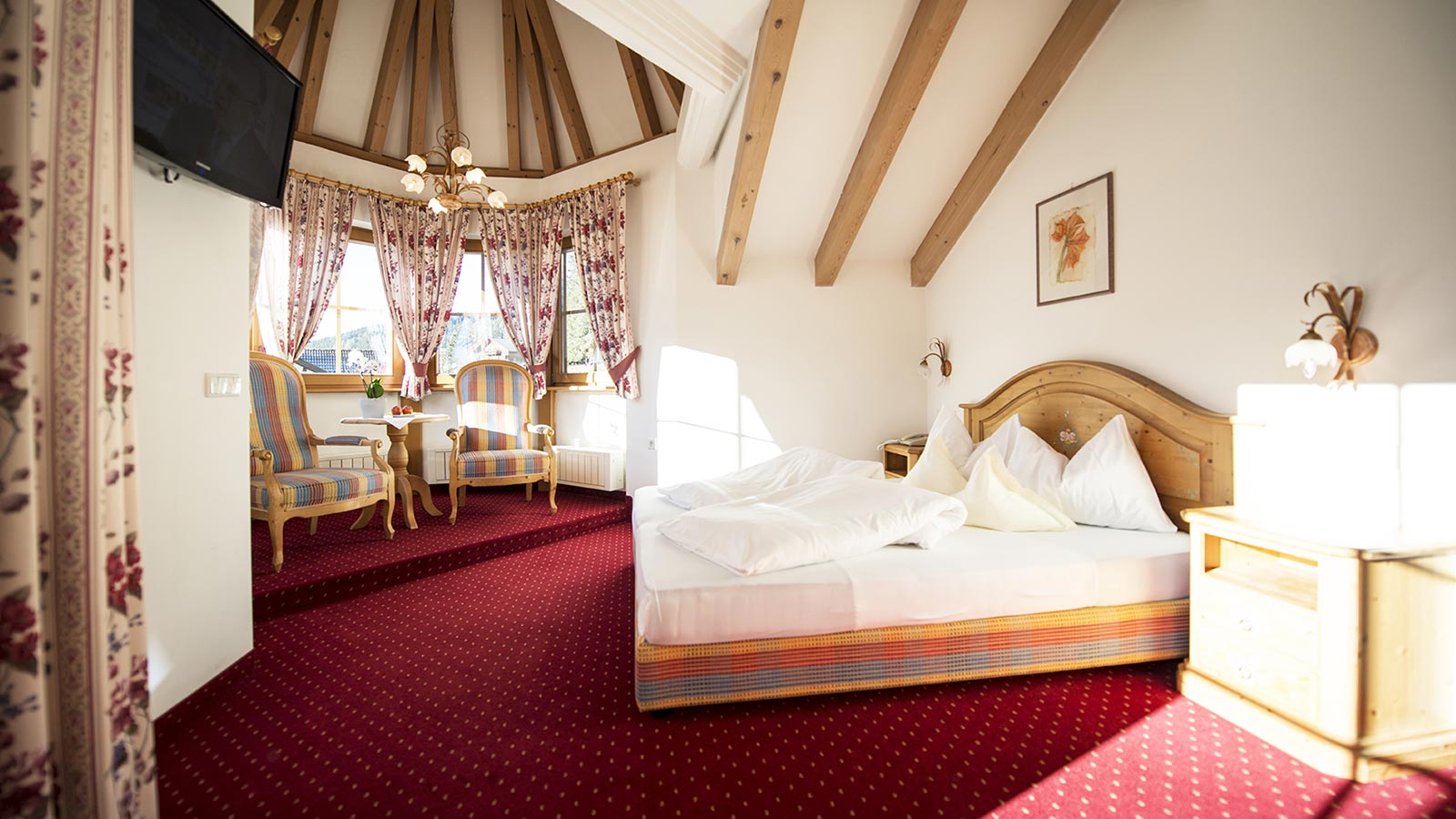 Raffinata e spaziosa camera dell'Hotel Gschwendt con moquette di colore rosso, letto matrimoniale e grandi finestre