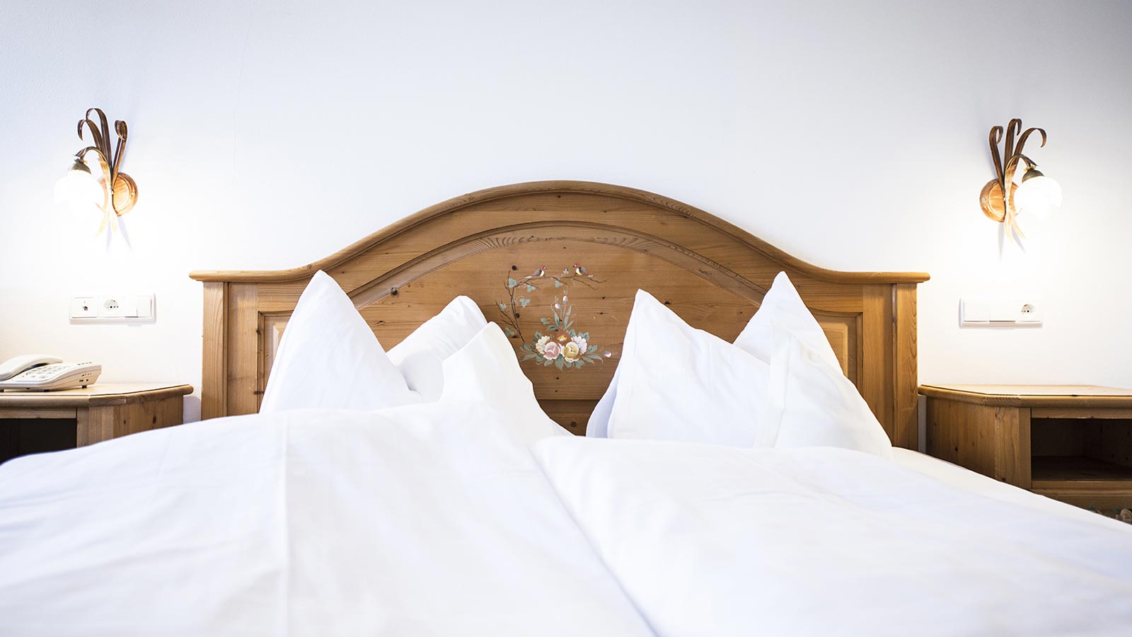 Doppelbett mit weißer Bettwäsche und zwei Leuchtern an der Wand
